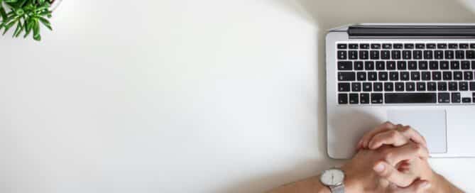 Person with clasped hands waiting in front of a laptop, suggesting a sense of waiting for approval