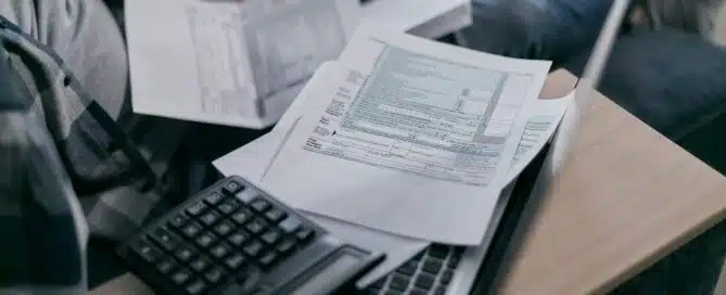 A person is working on invoice financing, with documents and a calculator placed on a laptop.